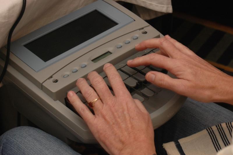 Two hands touch keys of a steno machine with screen