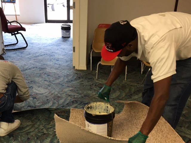 two men work on a floor, installing a hearing loop line under the carpet.