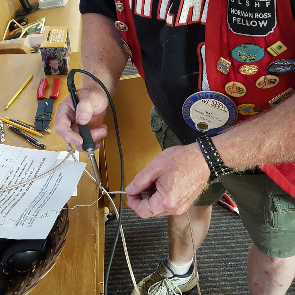 a closer photo as the man, with tools in hand, solders a wire.