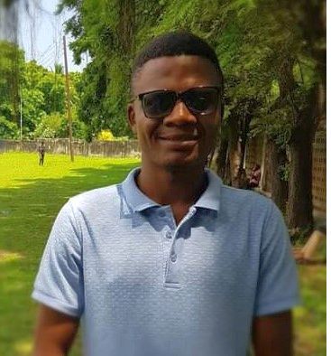 a dark-skinned man with sunglasses standing in a green forested area