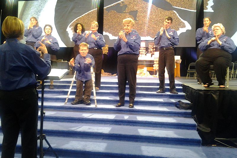 photo of Lovers Lane Sign Choir at General Conference; they are on short risers with a stylized globe in the background.