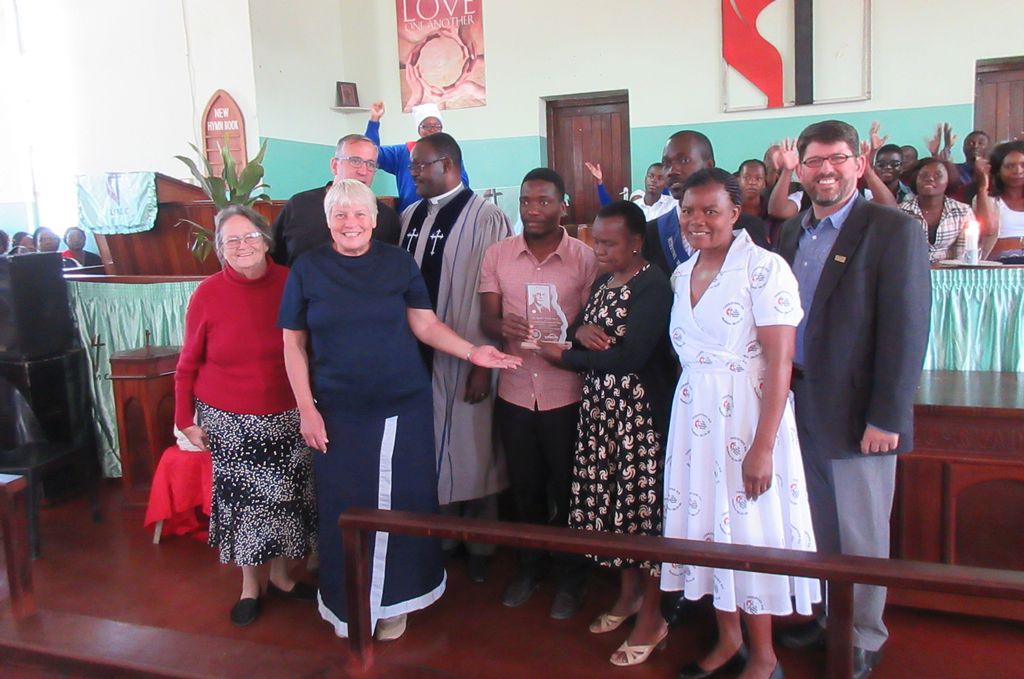 several people gather in front of a small church as plaque is presented.