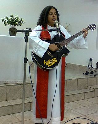 author, in pastor's robe with a red stole, plays guitar