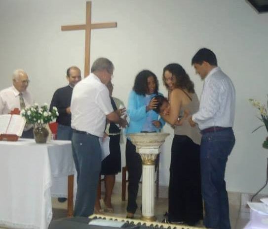 the author baptizing a young child at a font, surrounded by family