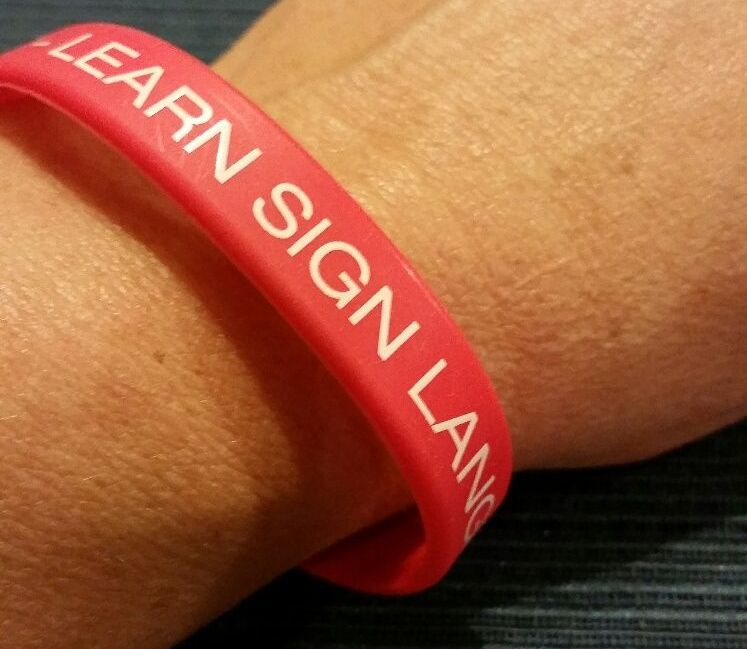 a red plastic bracelet on a wrist, it reads Learn Sign Language.