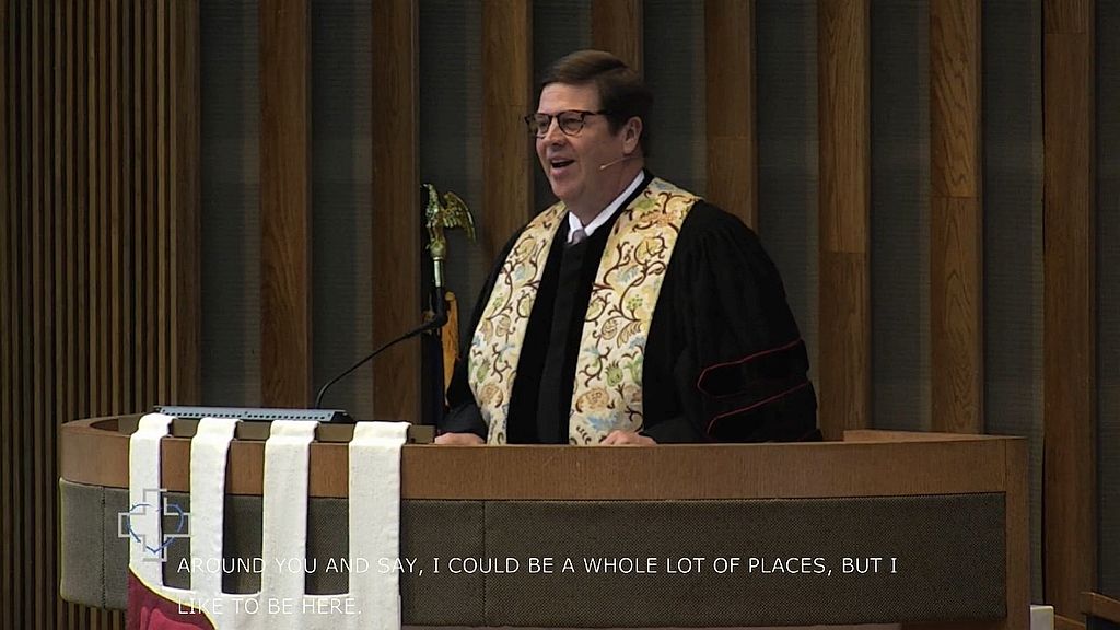 man in pulpit speaking with caption stream undernearth