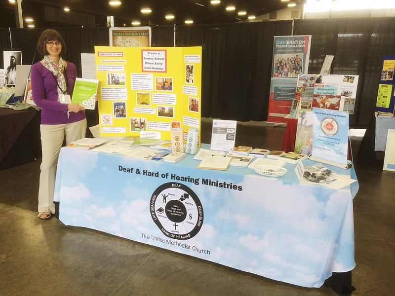 photo showing Lynn Swedberg standing next to a table, the table has a display of Deaf and hard-of-hearing activities.